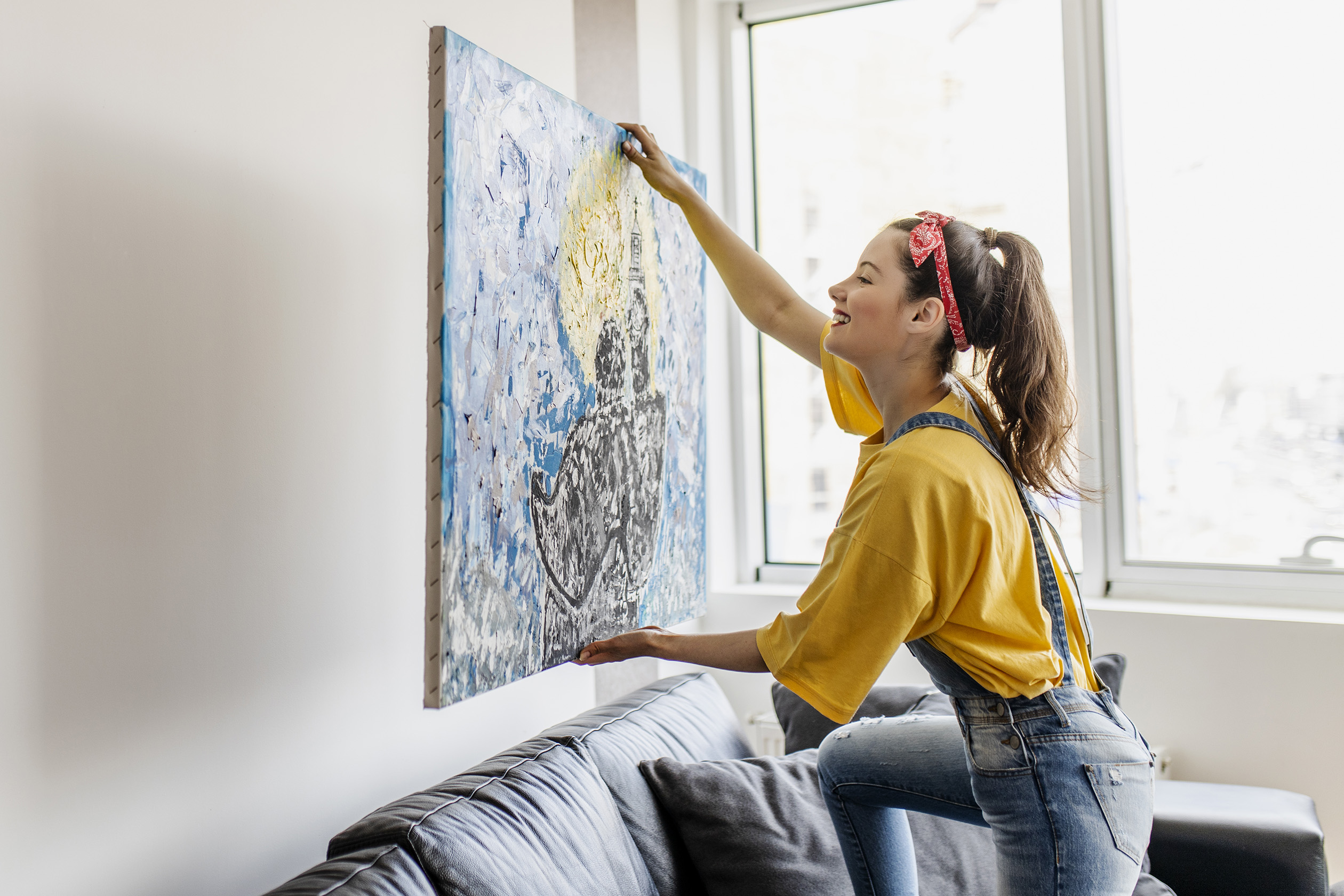 Woman hanging art on wall behind couch