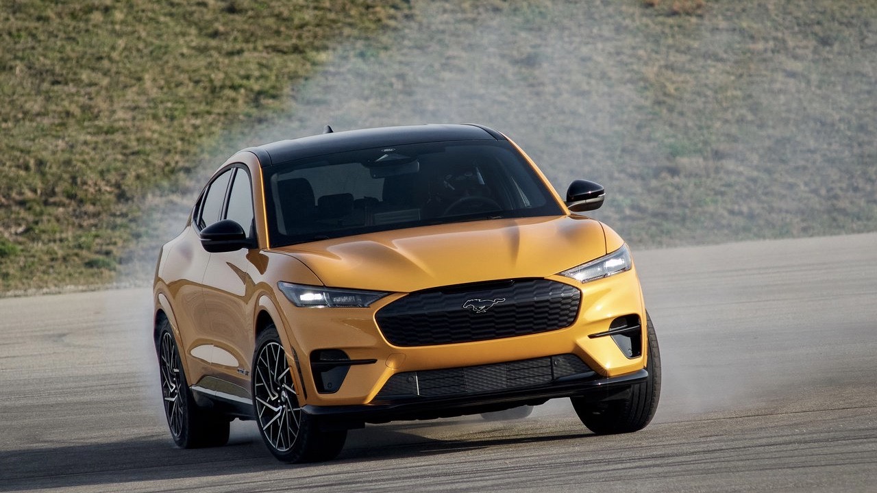 Front view of a moving yellow Ford Mustang Mach-E EV maneuvering at speed.
