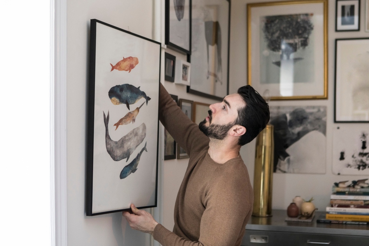 man hanging artwork in his home for his design scheme