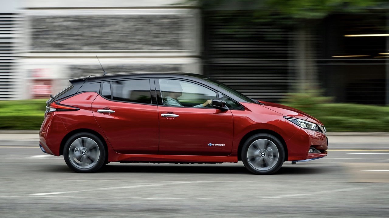 Side view of a moving red NIssan Leaf.