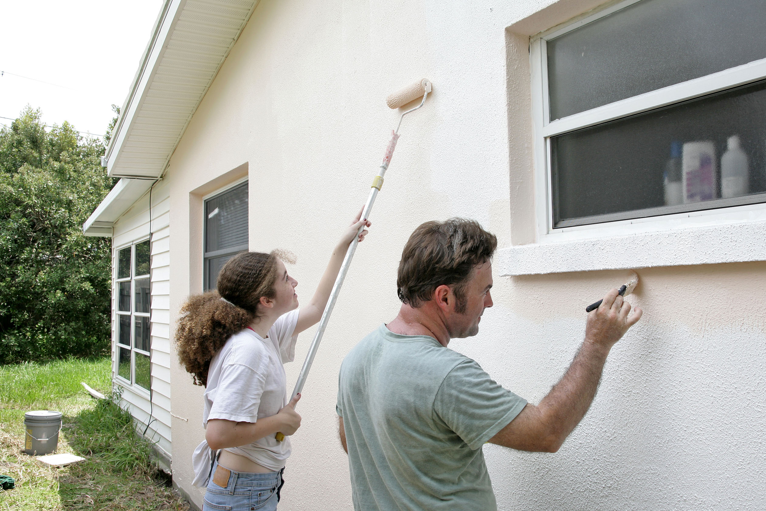 Father and daughter painting exterior of house
