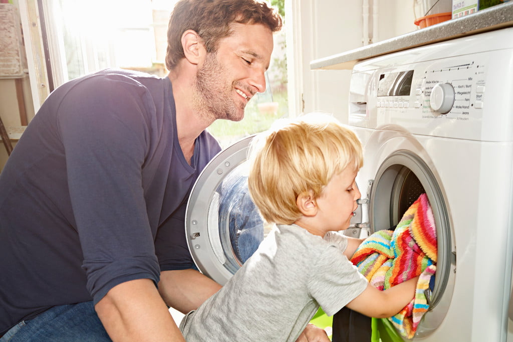 Father and young son putting laundry in the dryer