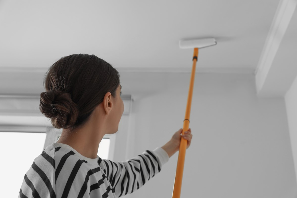 Woman in striped shirt painting ceiling with extended roller