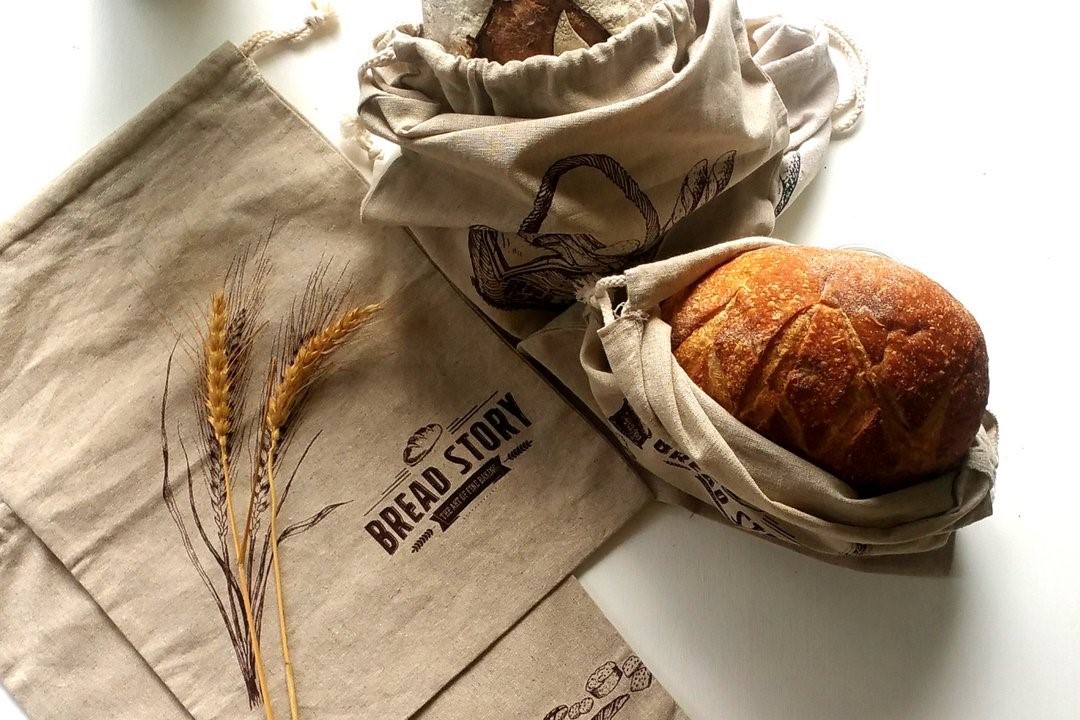 Loaf of bread and empty Bread Story Natural Linen Bread Bags on white countertop