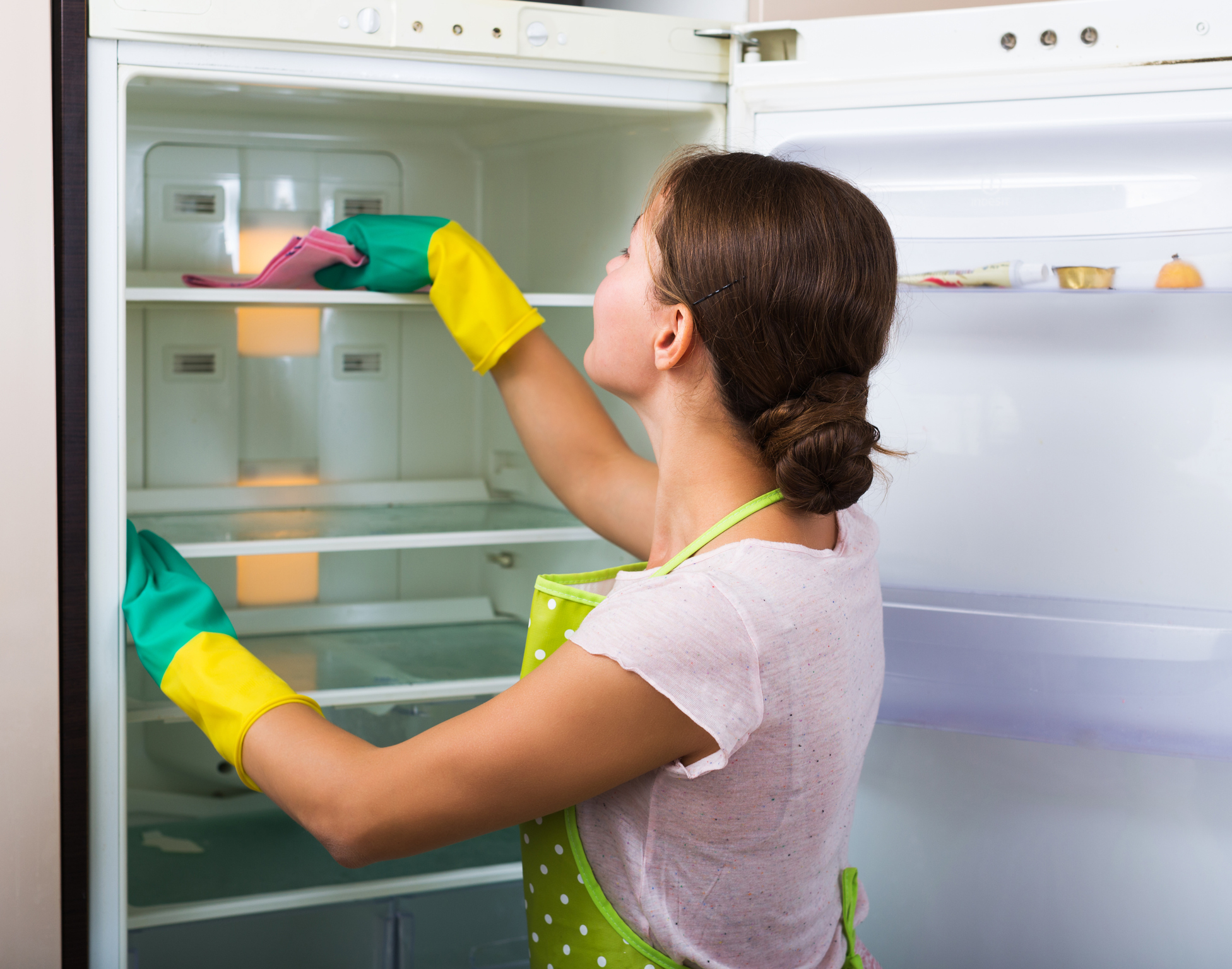 Woman in yellow gloves cleaning refrigerator
