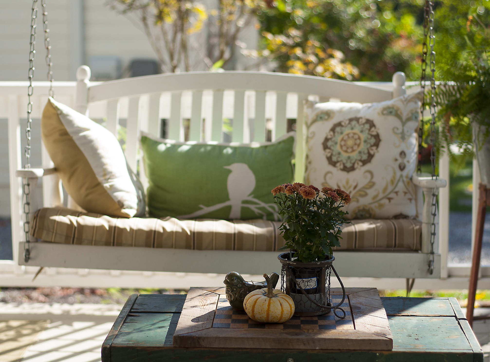 porch swing with pillows on it and small table in front