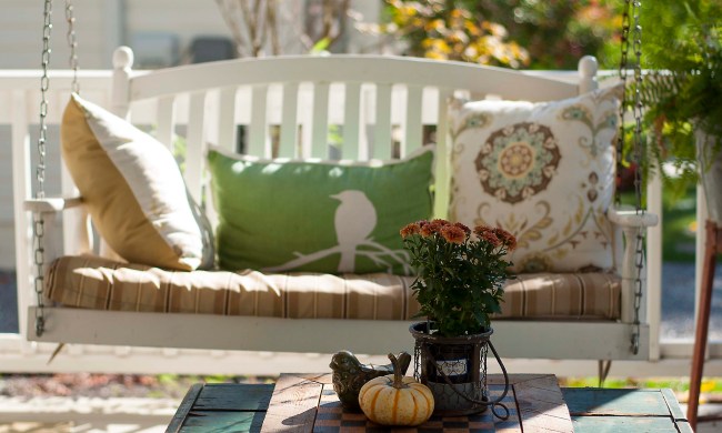 Porch swing with pillows on it and small table in front