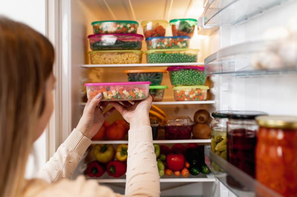 Woman standing in front of refrigerator filled with storage containers of food