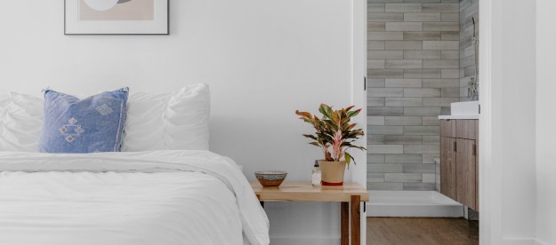 A white-covered bed sits against a white wall with exposed brick in the background.
