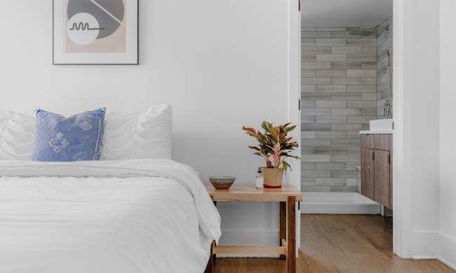 A white-covered bed sits against a white wall with exposed brick in the background