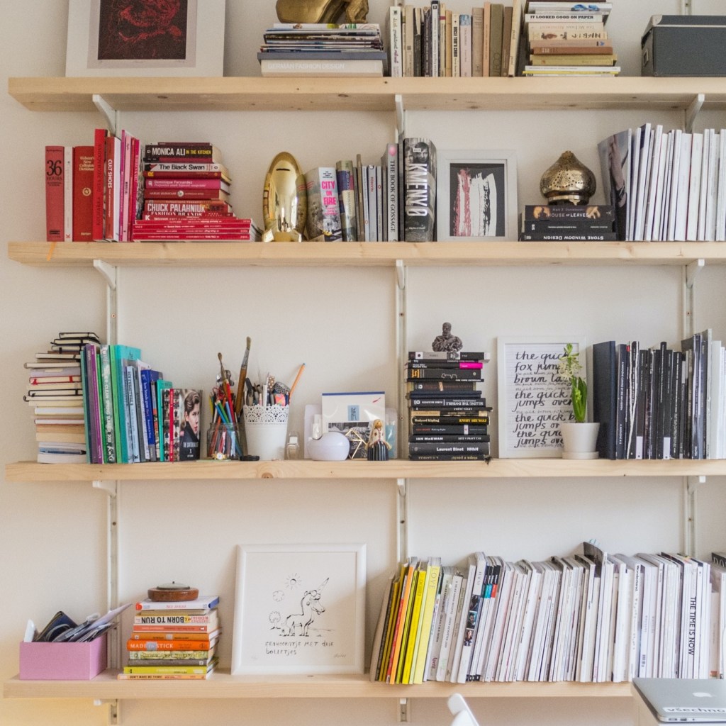A light wooden bookshelves climb a white wall