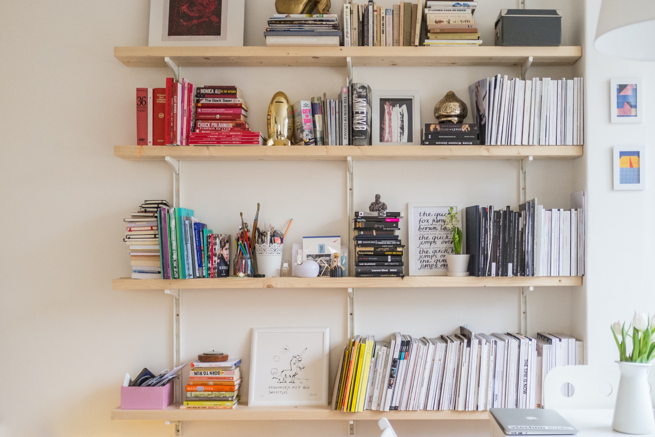 A light wooden bookshelves climb a white wall