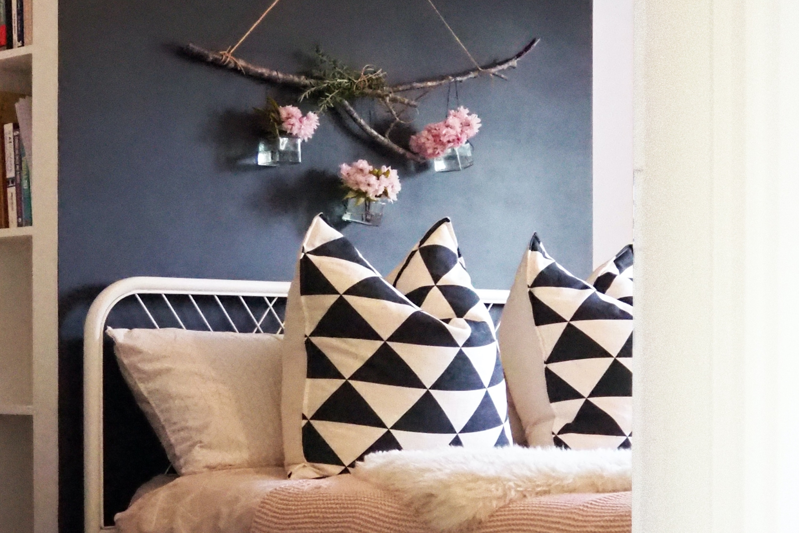 Flowers hang on a statement wall above a white-framed bed with navy blue and white pillows