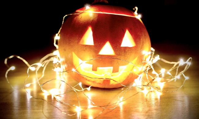 Lit up pumpkin sits on a wooden surface covered by fairy lights