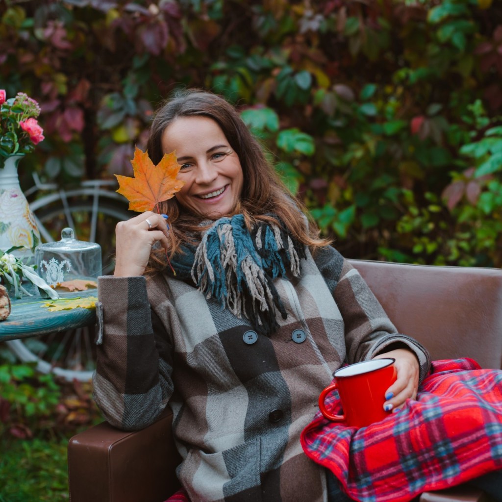 Woman on patio holding a leaf and mug with checkered blanket on lap