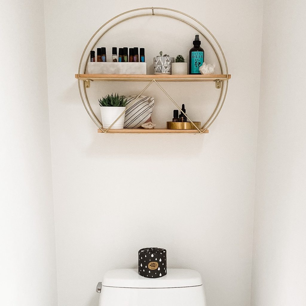 A shelf hanging over a toilet stores bathroom items.