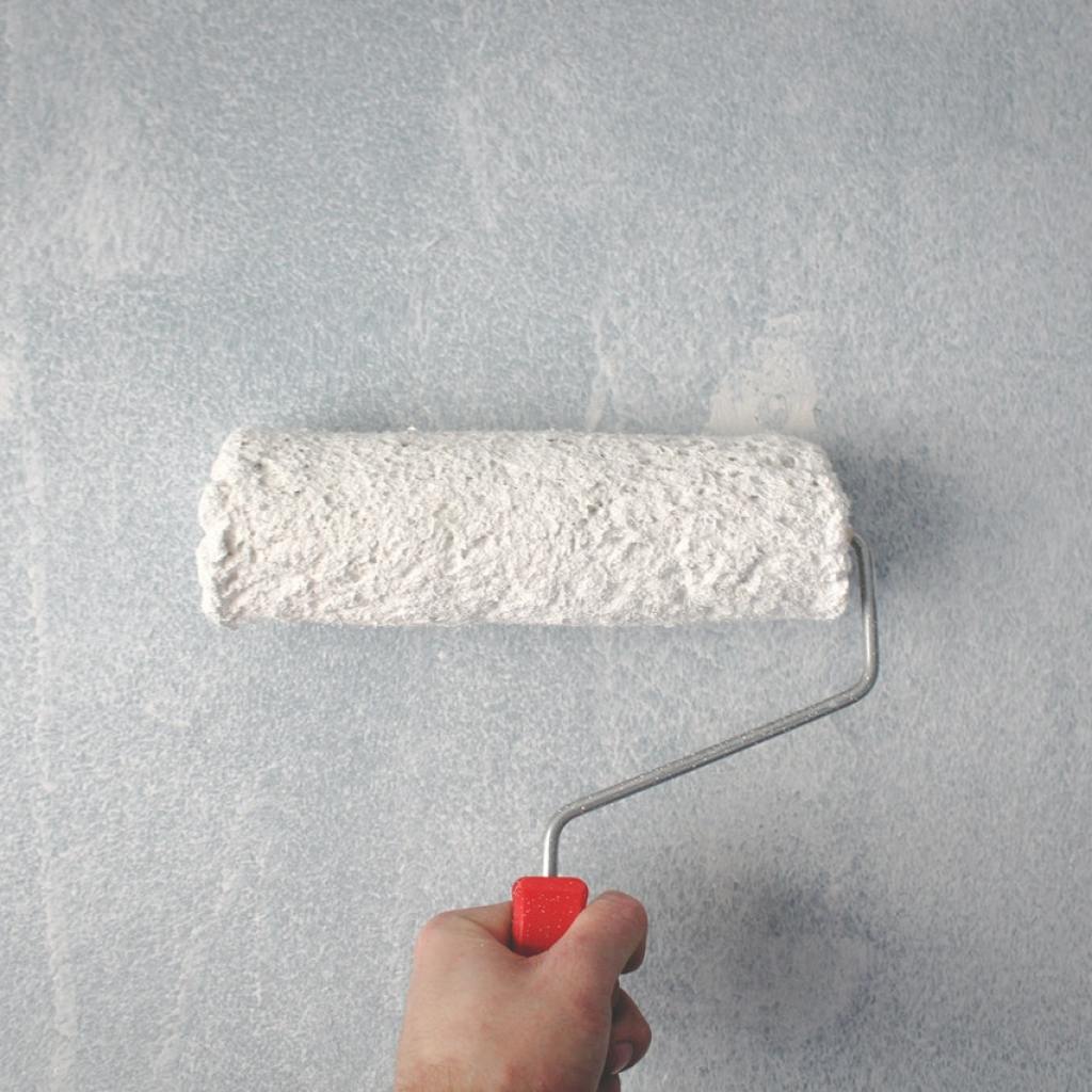 Hand holding paint roller against white wall