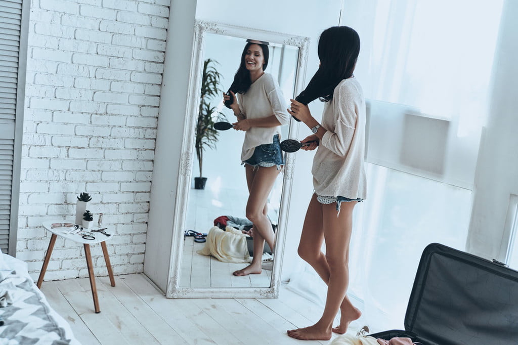 Young woman brushing hair in front of full length mirror