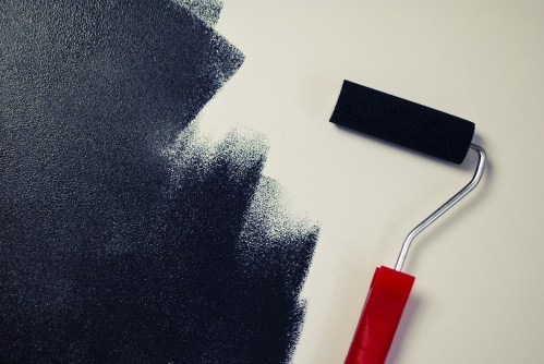 Red roller brush with black paint on white wall