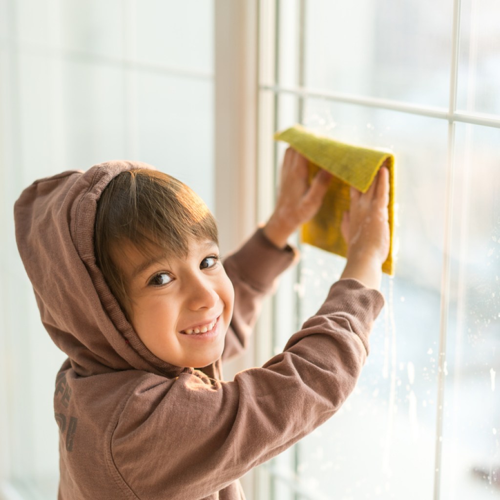 A young boy washing windows with a cloth