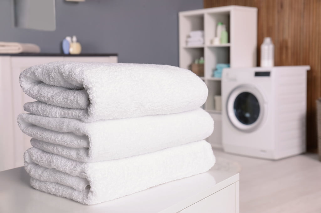 Three white towels stacked on table with washing machine in background