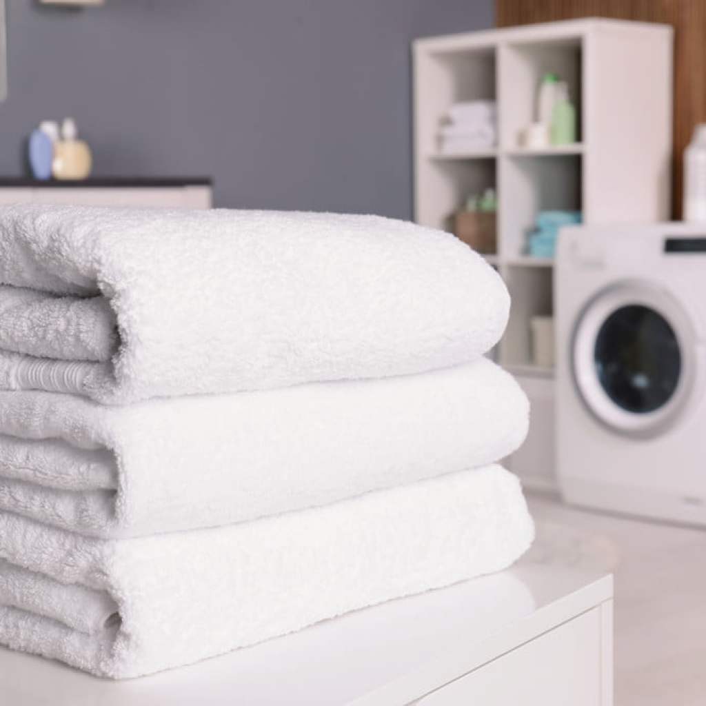 Three white towels stacked on table with washing machine in background