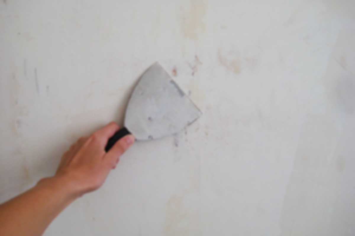 Person with putty knife patching drywall