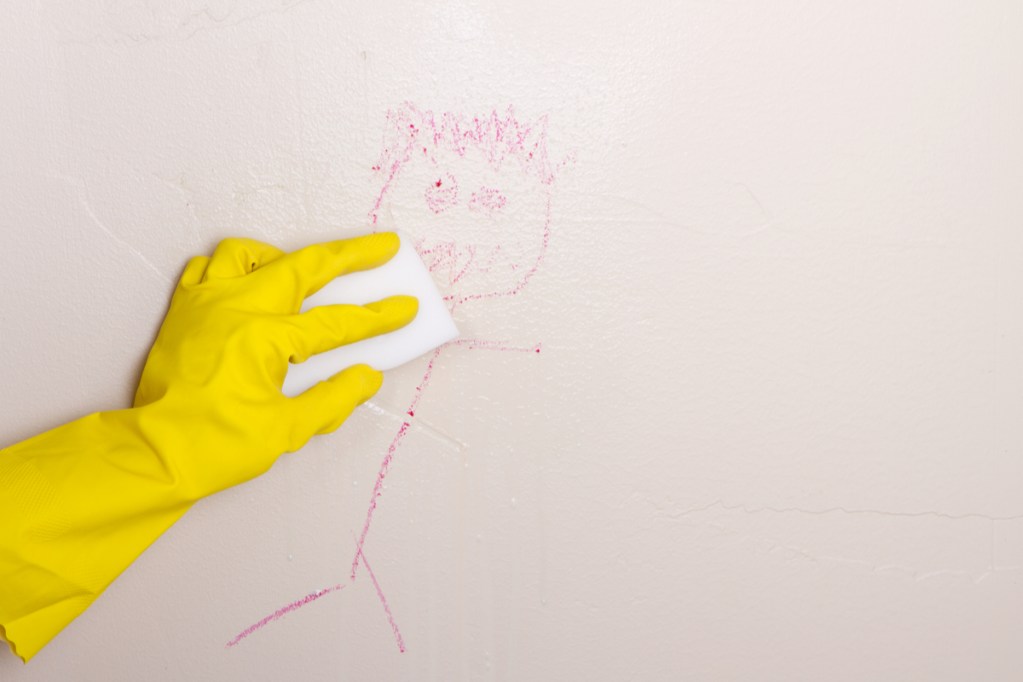 Gloved hand cleaning crayon off wall with a Magic Eraser