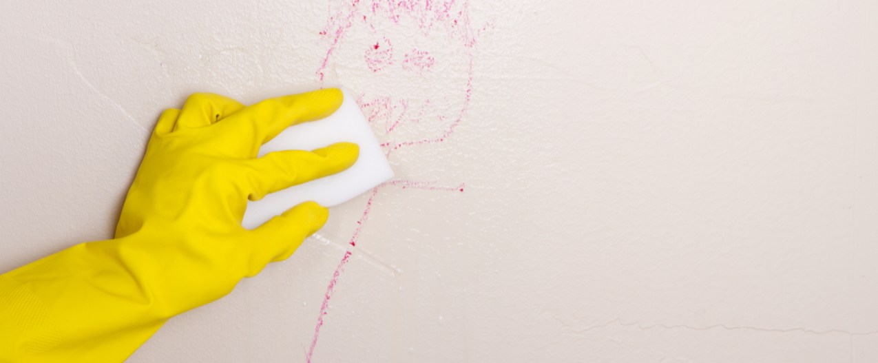 Gloved hand cleaning crayon off wall with a Magic Eraser