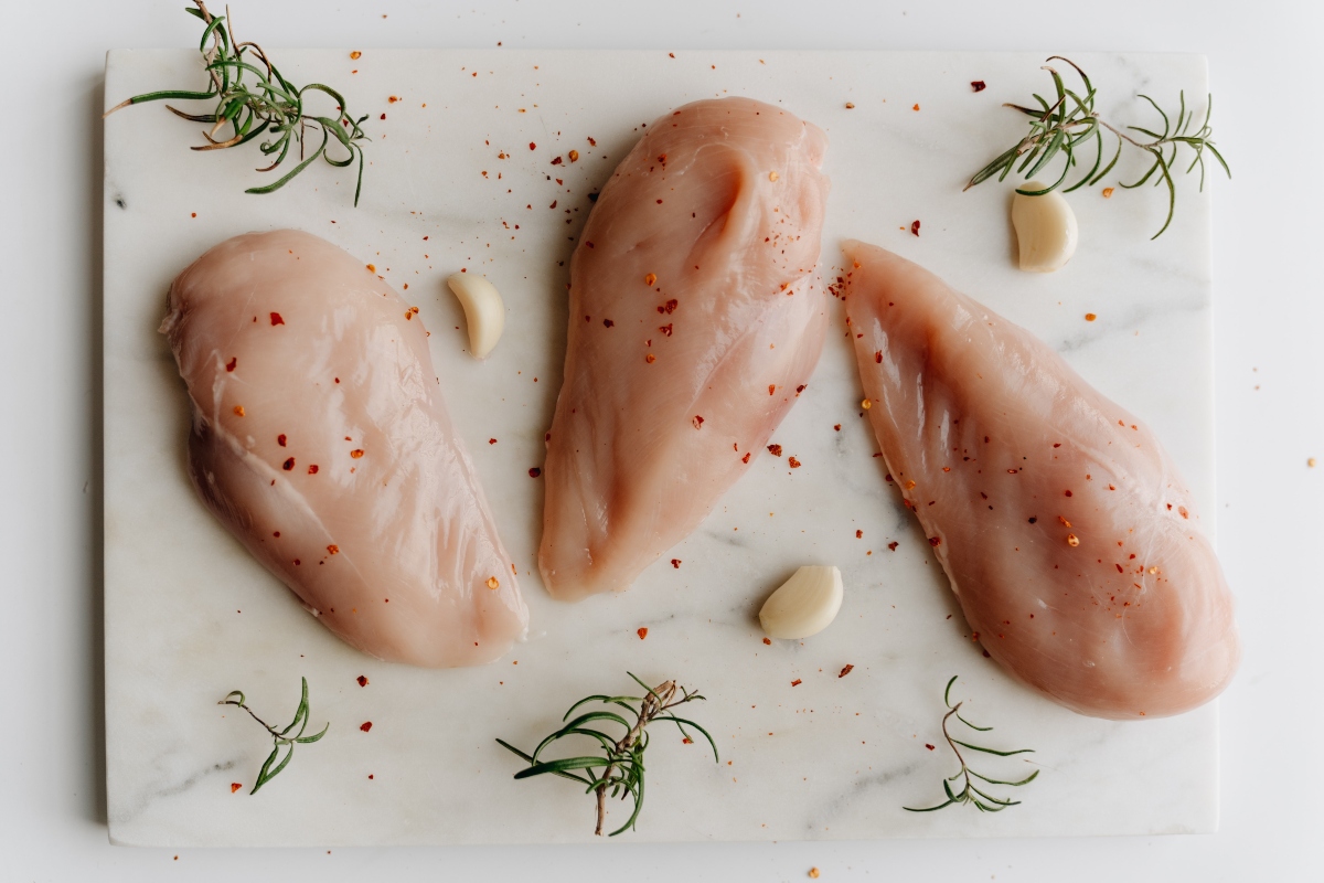 Raw chicken breasts surrounded by seasonings on a white surface