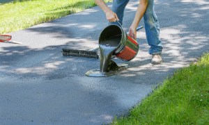 man applying asphalt sealant on a driveway