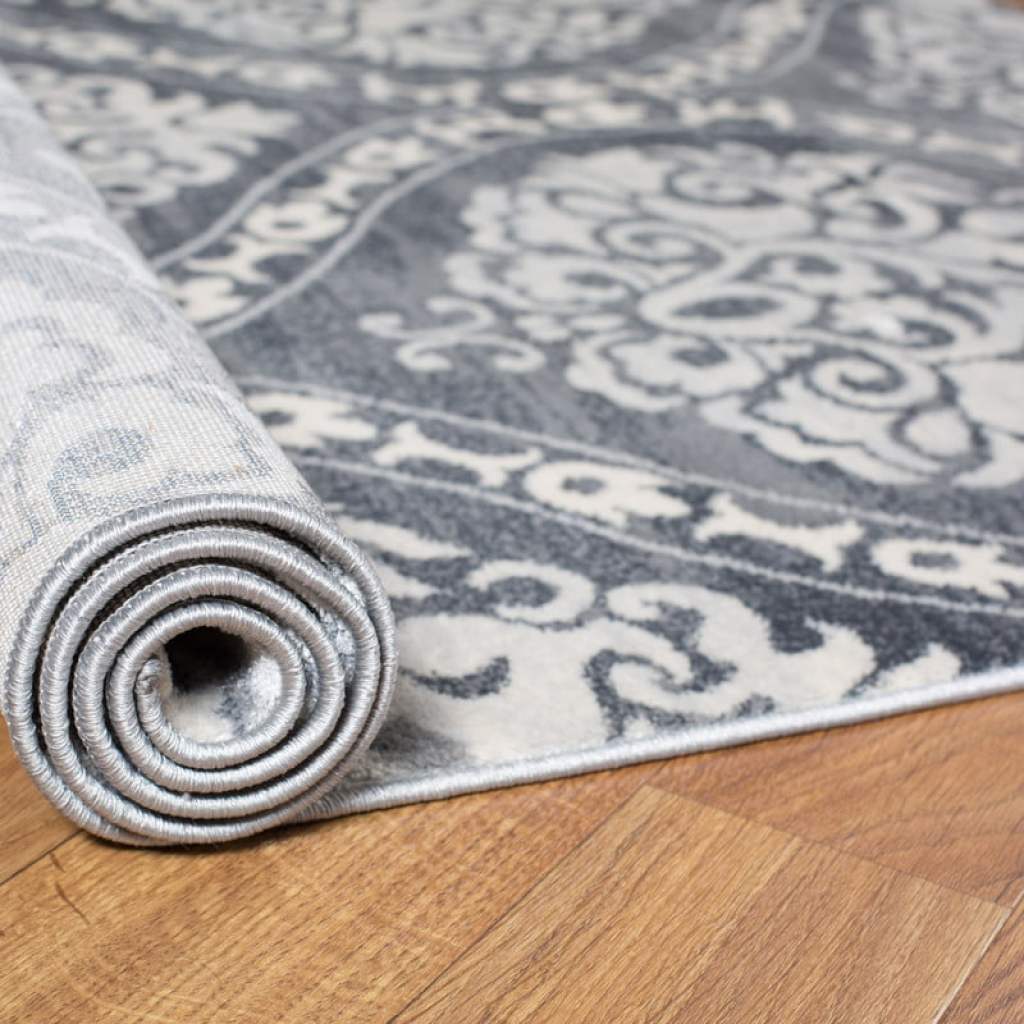 gray patterned rug being rolled out onto wood floor