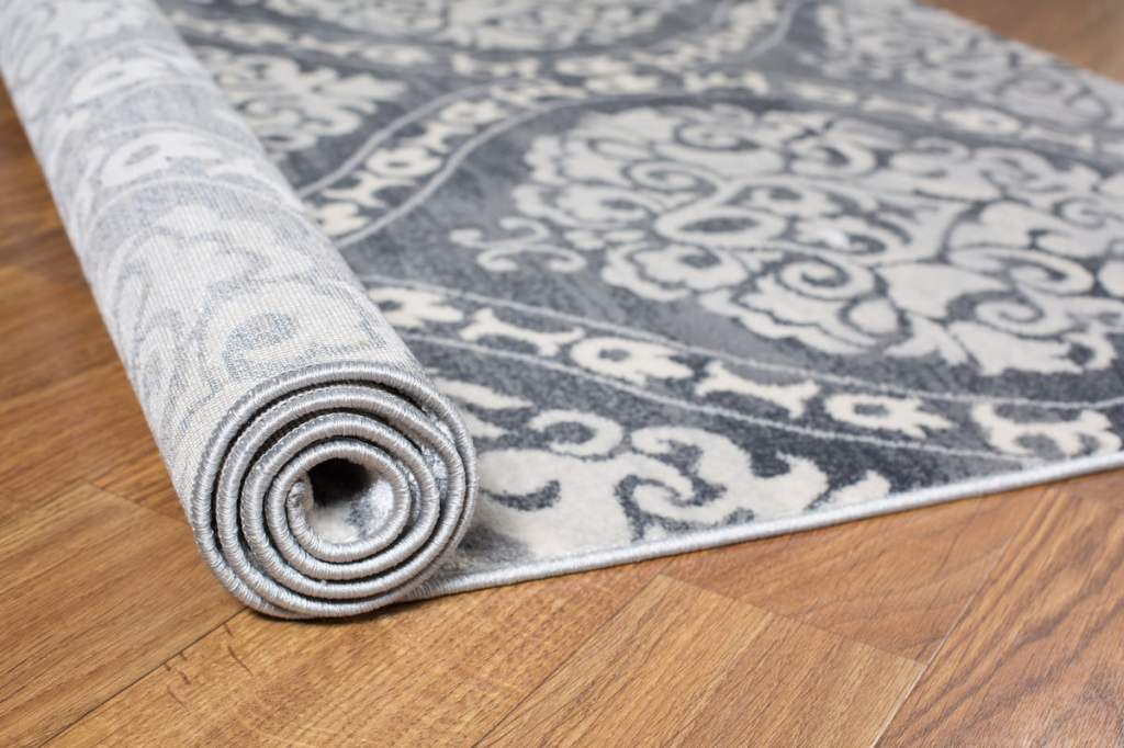gray patterned rug being rolled out onto wood floor