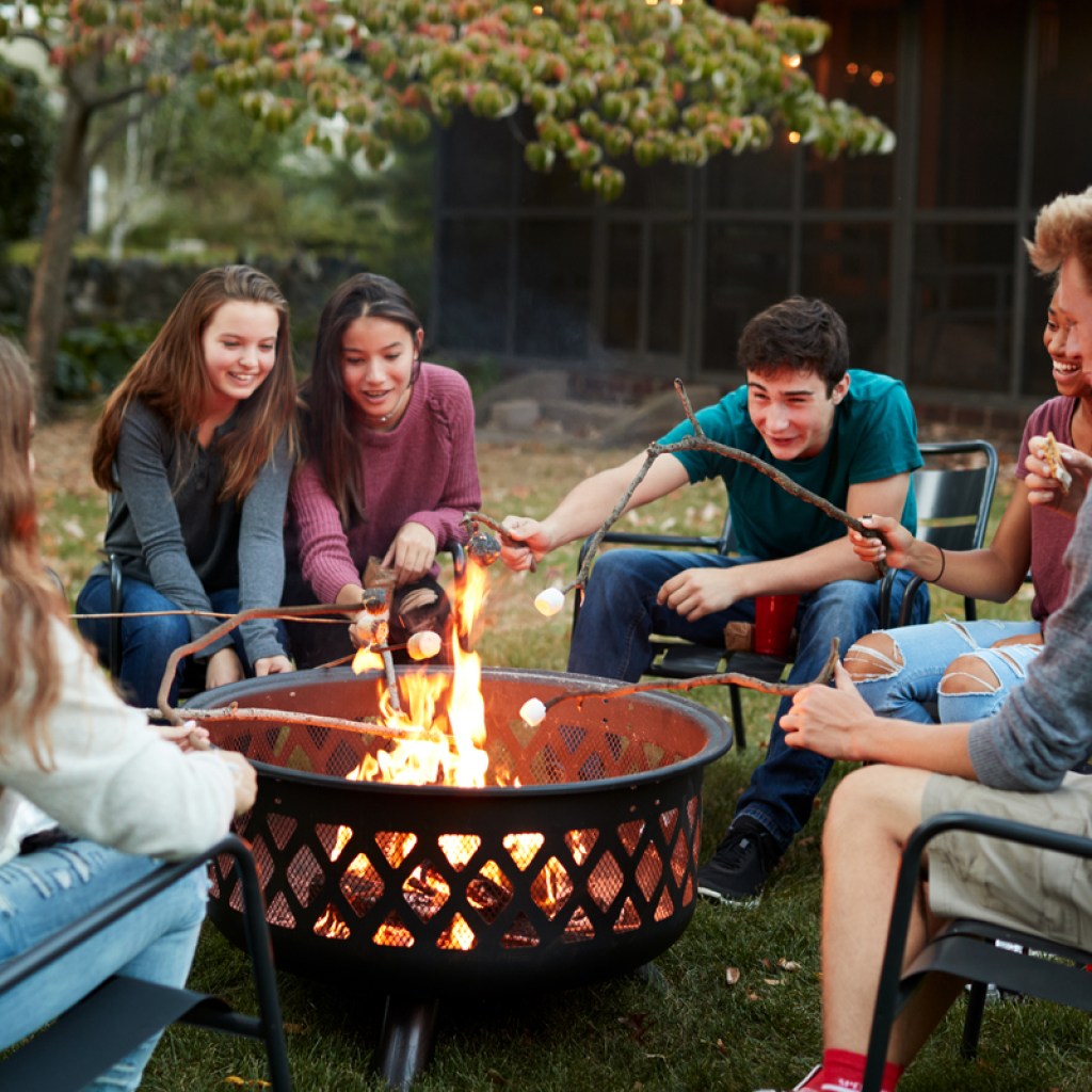 teenage friends toasting marshmallows around a fire pit