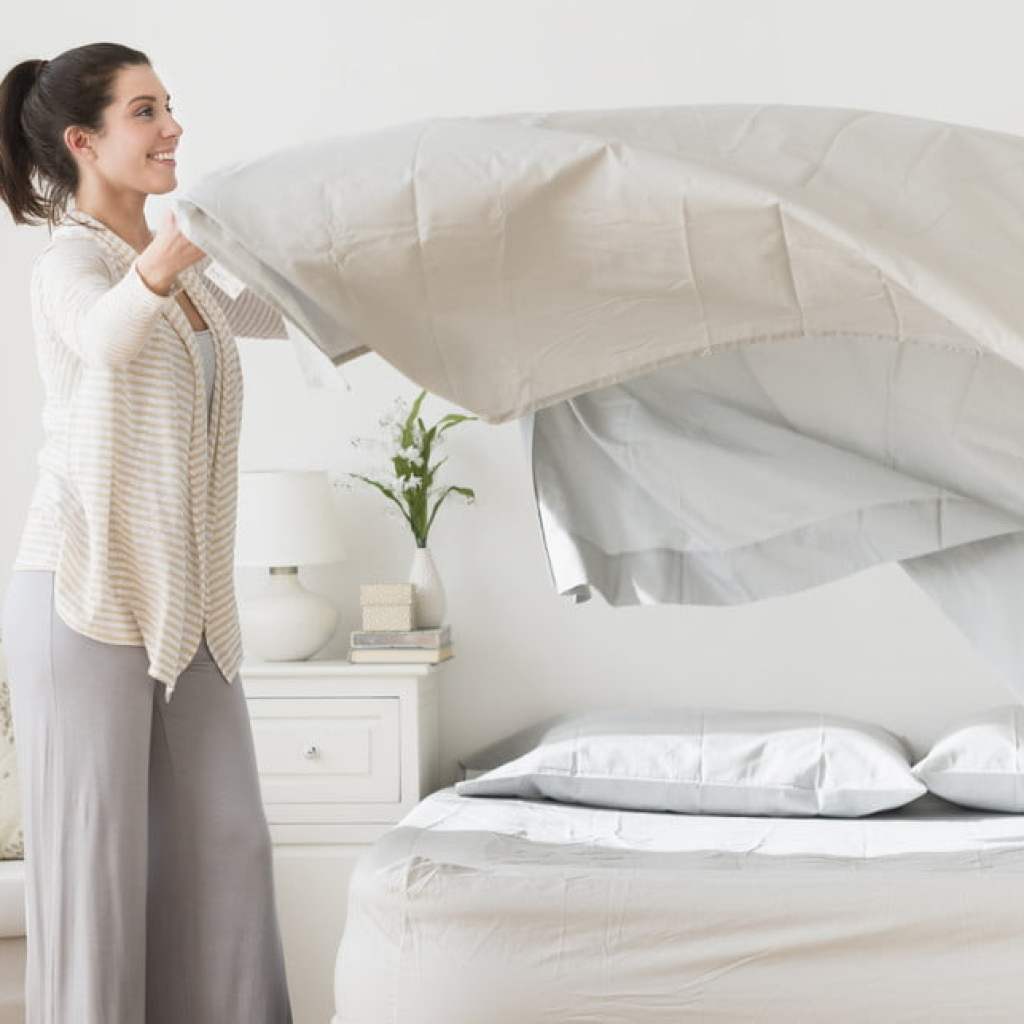 Woman putting white sheets on a bed