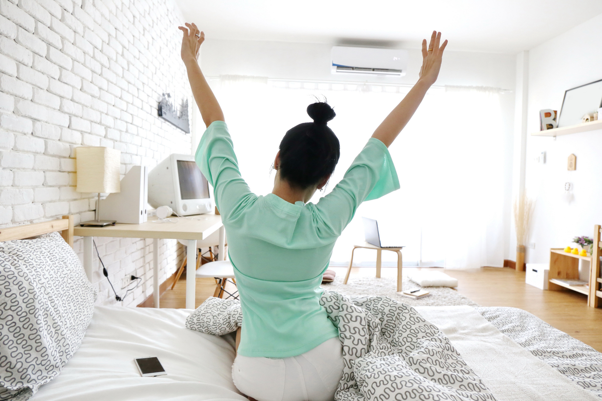 woman stretching in bed with ac unit on wall