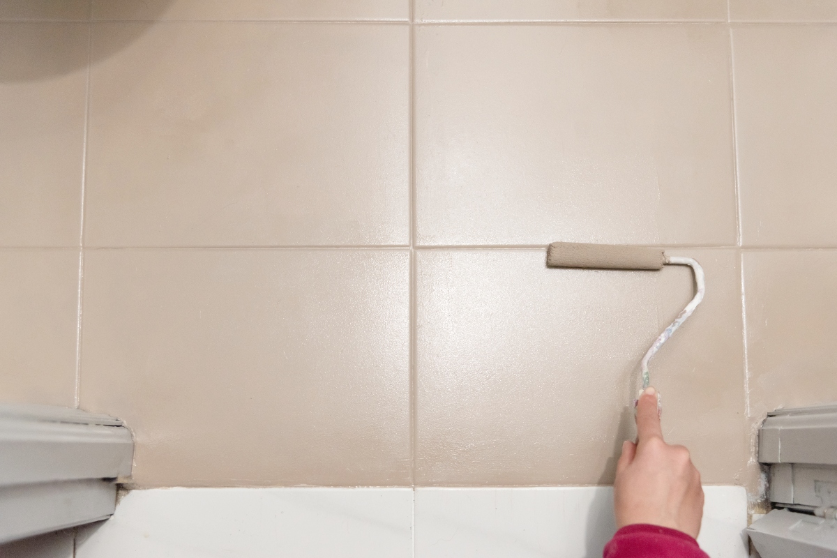 person painting bathroom floor tiles with roller