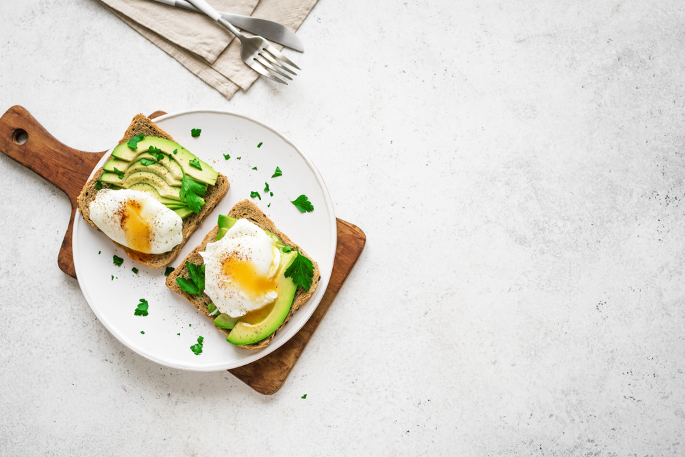 Avocado toast with eggs on white plate and table
