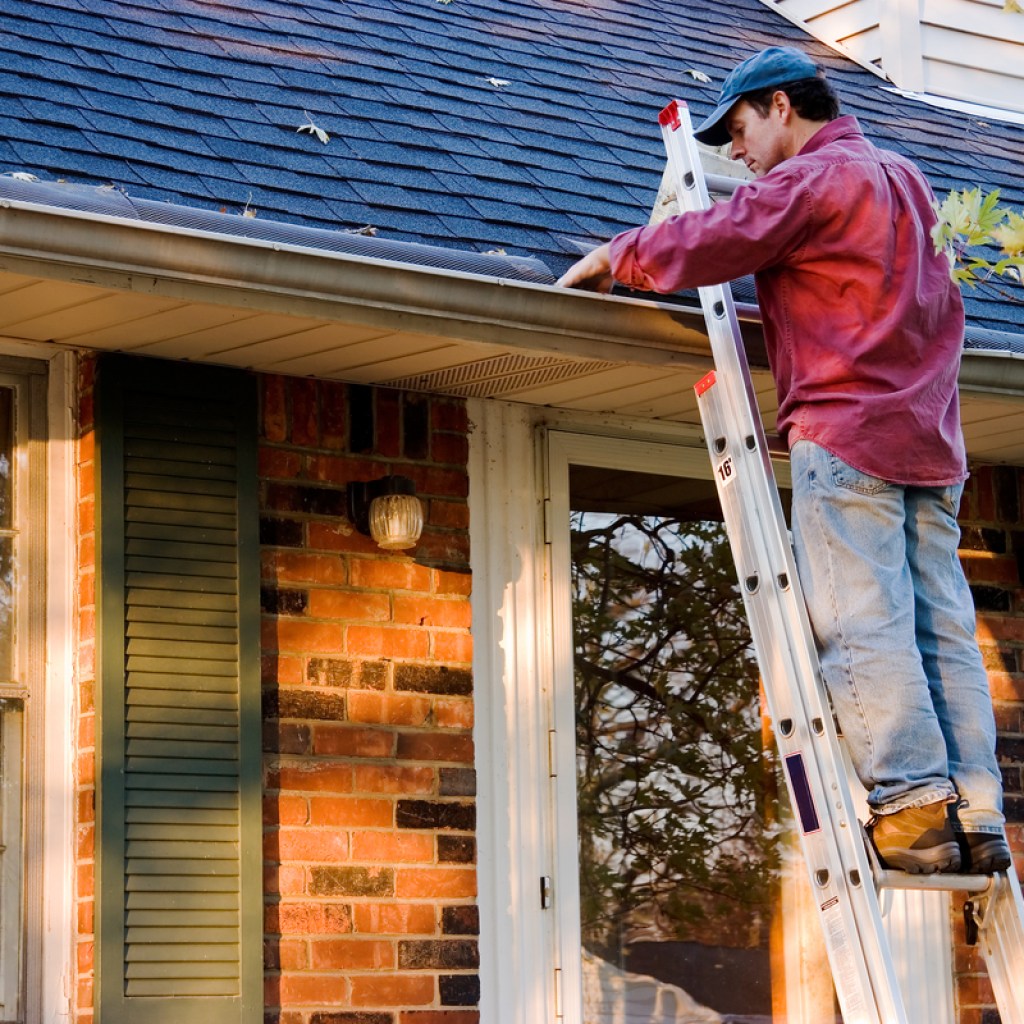 man on a ladder cleaning rain gutters