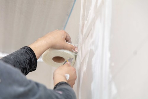 Person using drywall tape to repair drywall