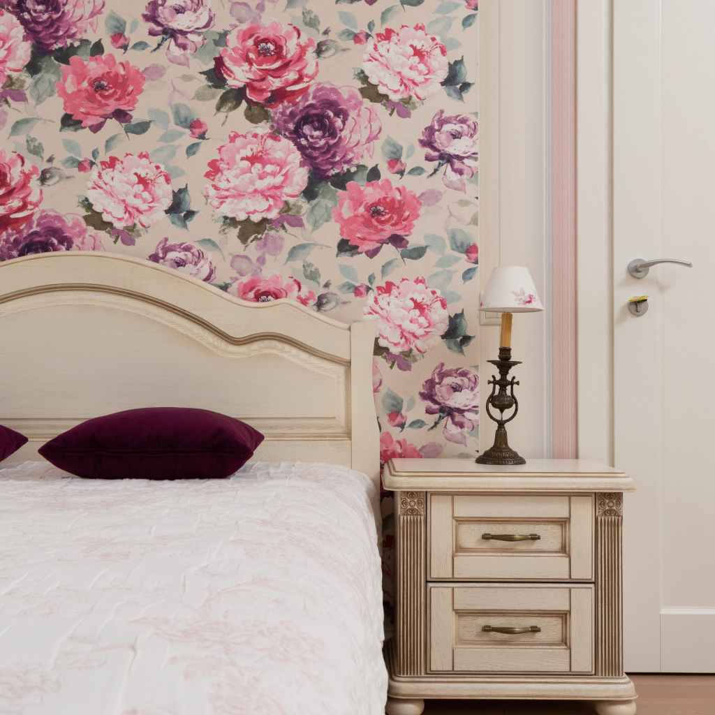 Bedroom with floral wallpaper and lamp on nightstand.