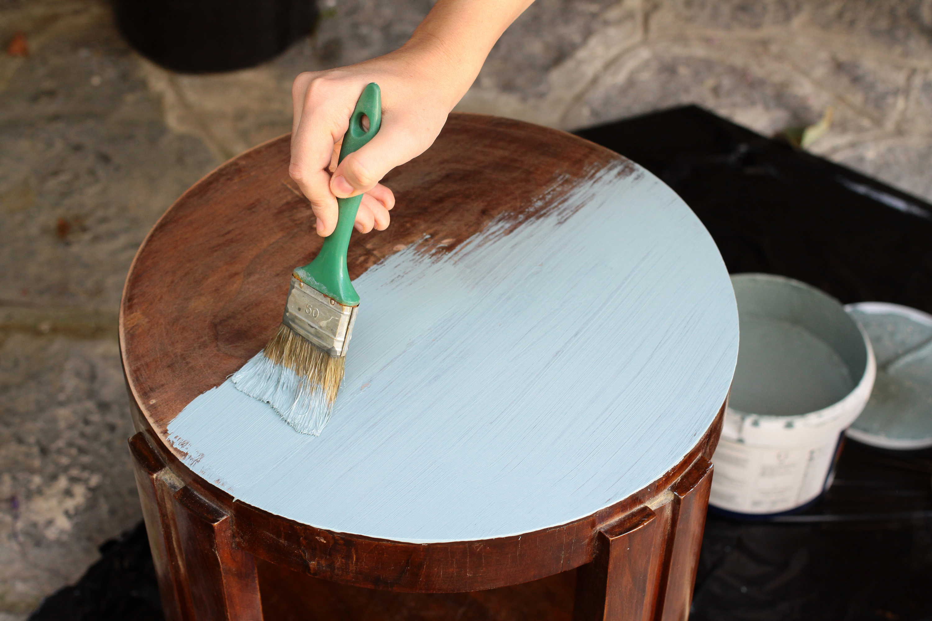 Woman's hand staining a stool with paintbrush