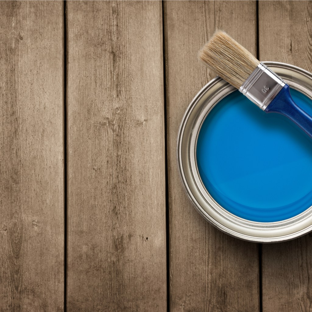Small blue paint can with paint brush set on top.