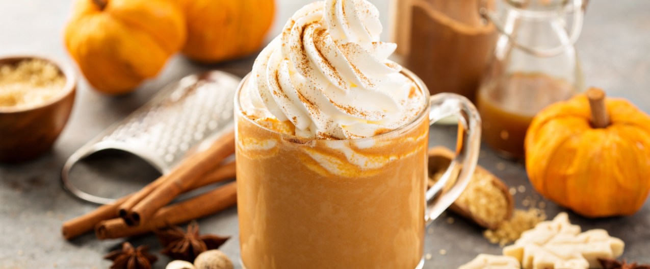 Pumpkin spice latte on a table with pumpkins, cinnamon sticks, and other fall items