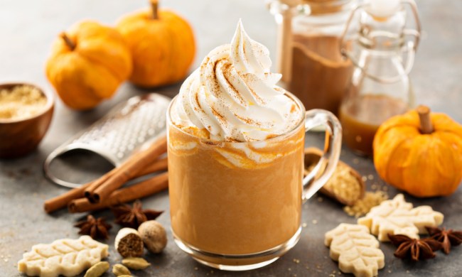 Pumpkin spice latte on a table with pumpkins, cinnamon sticks, and other fall items