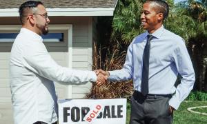 two men shaking hands in front of a sold house sign