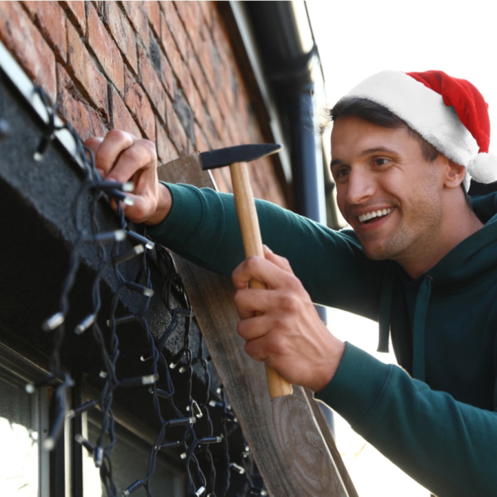 Man attaching Christmas lights around a window