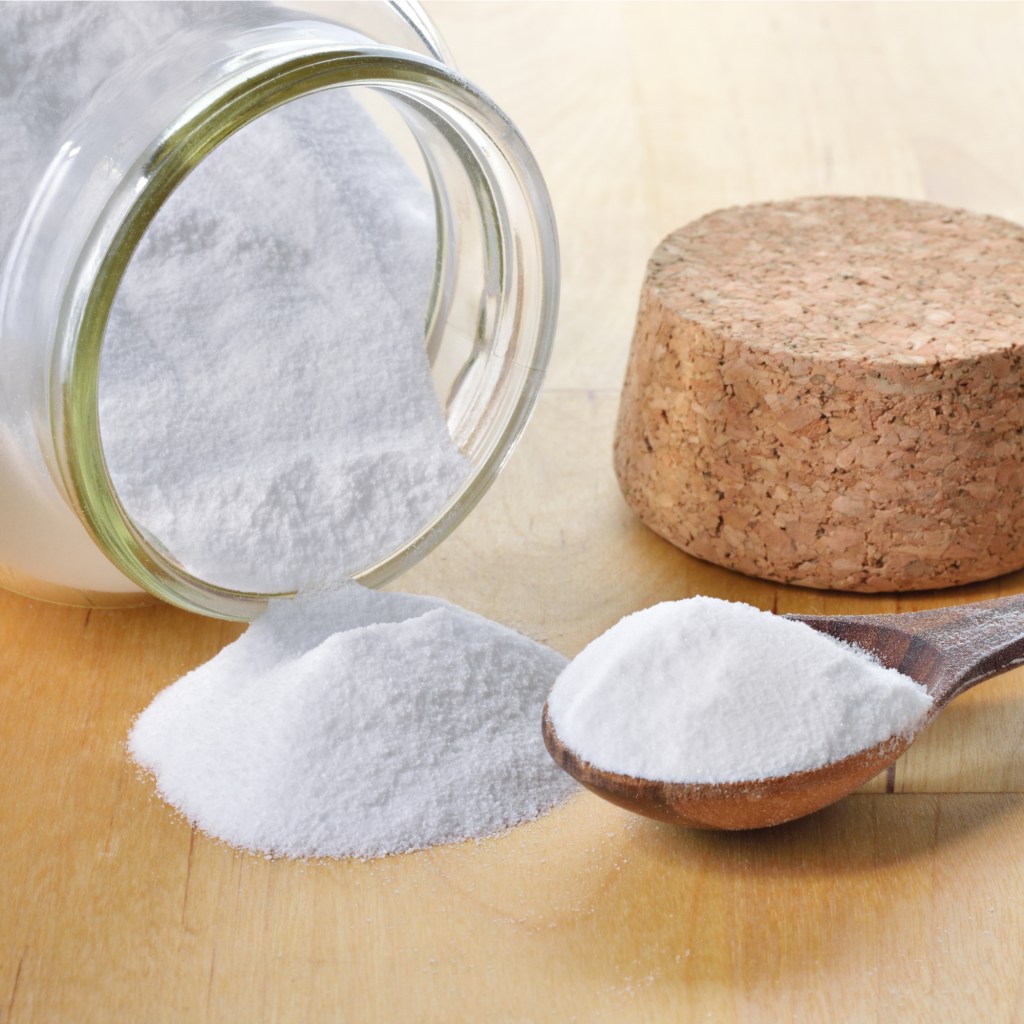 Glass jar of baking soda with cork and teaspoon tipped over.