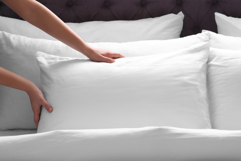 person fluffing pillow on the bed