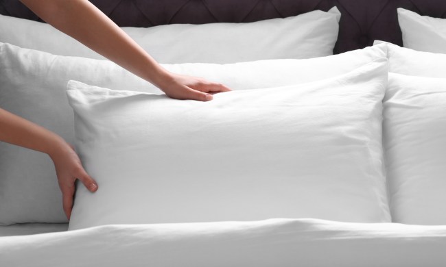 Person fluffing a pillow on the bed